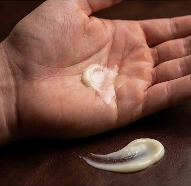Hand holding a small amount of cream on a dark surface